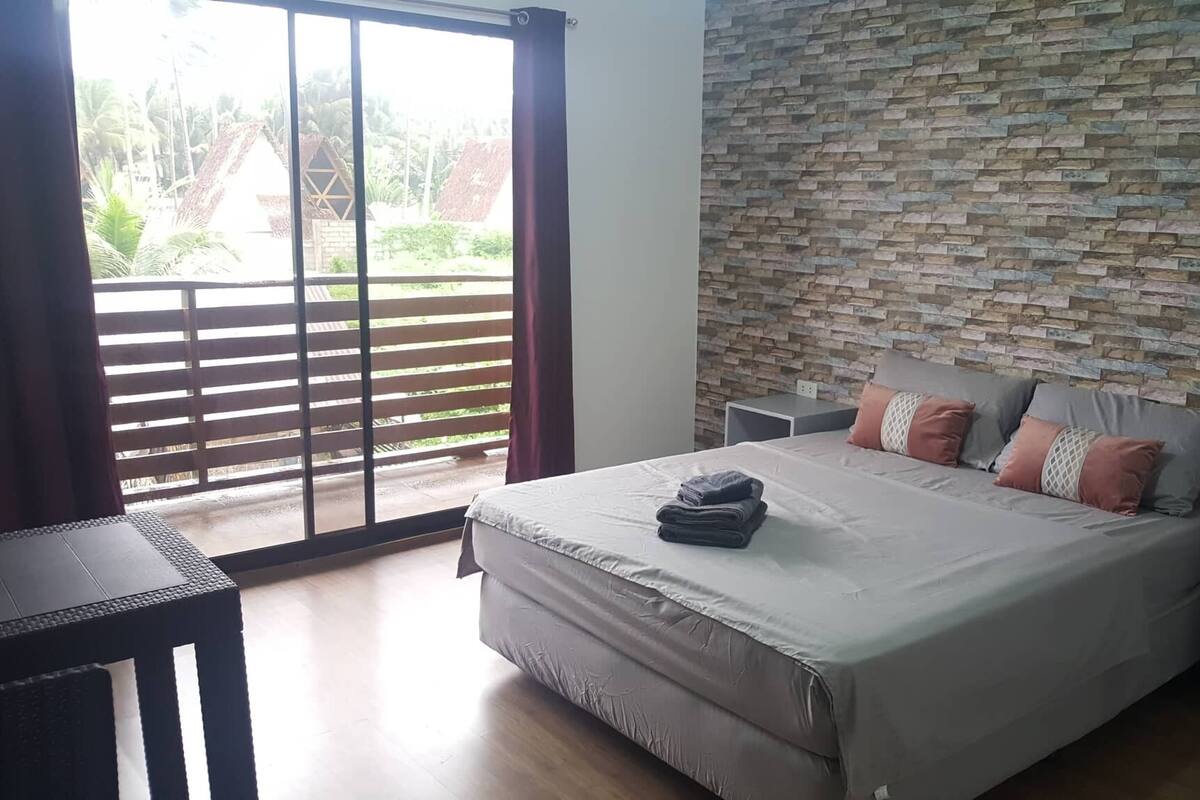 A bedroom with a bed, a nightstand, a table, and a view through a sliding door to an outdoor area.