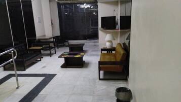 Quarto de hotel com sofá, mesa de centro, televisão e abajur.