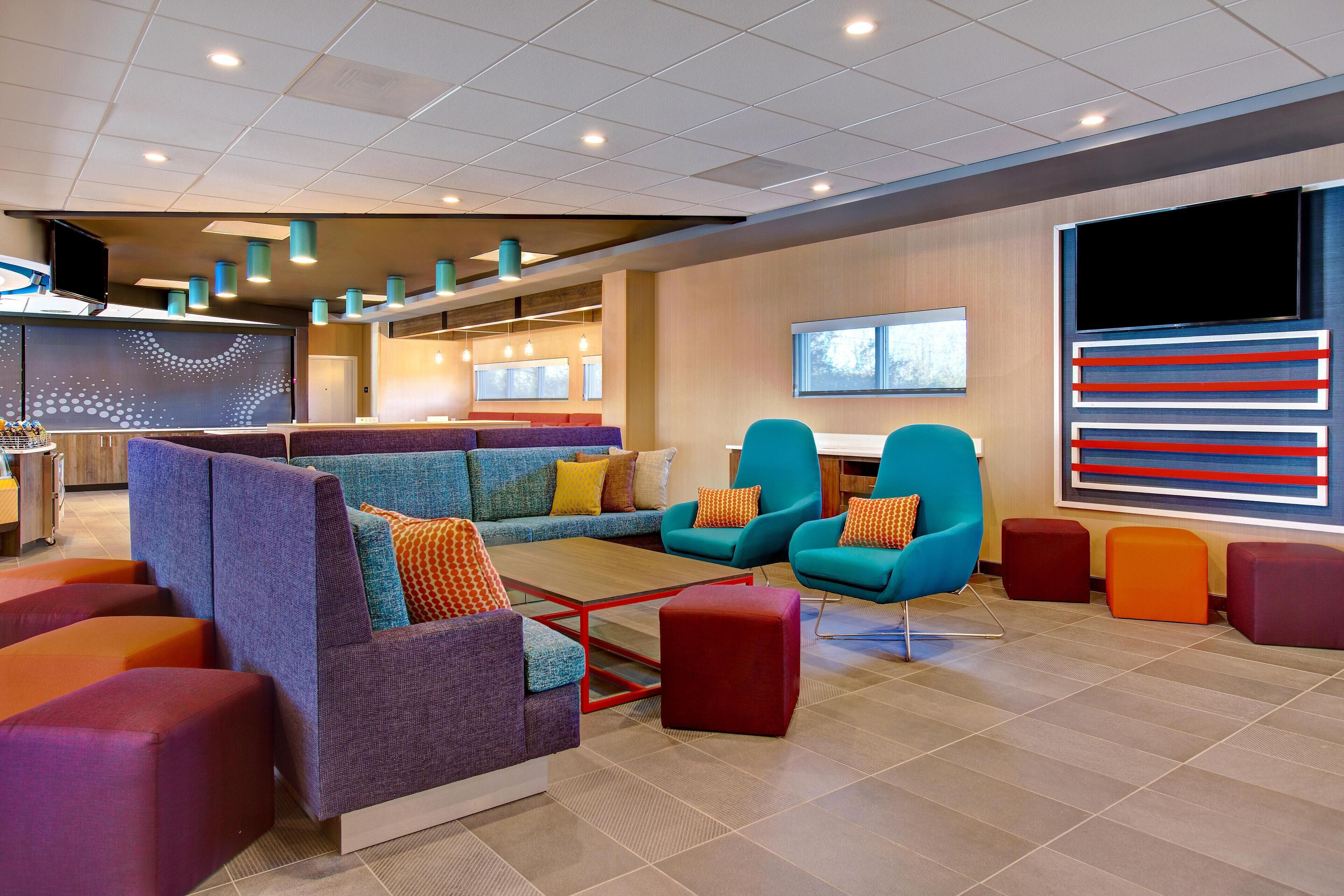A modern lobby with a sectional sofa, teal armchairs, and colorful ottomans.