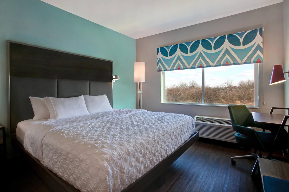 A hotel room with a large bed, a desk, and a window with a view of trees.