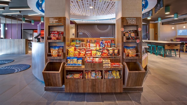 A snack kiosk with a variety of chips and snacks, a sign for 'eat. & sip. 2477 MARKET', and a 'CHECK OUT OUR LOCAL ITEMS' sign. - Tru by Hilton Alcoa Knoxville Airport (Alcoa)