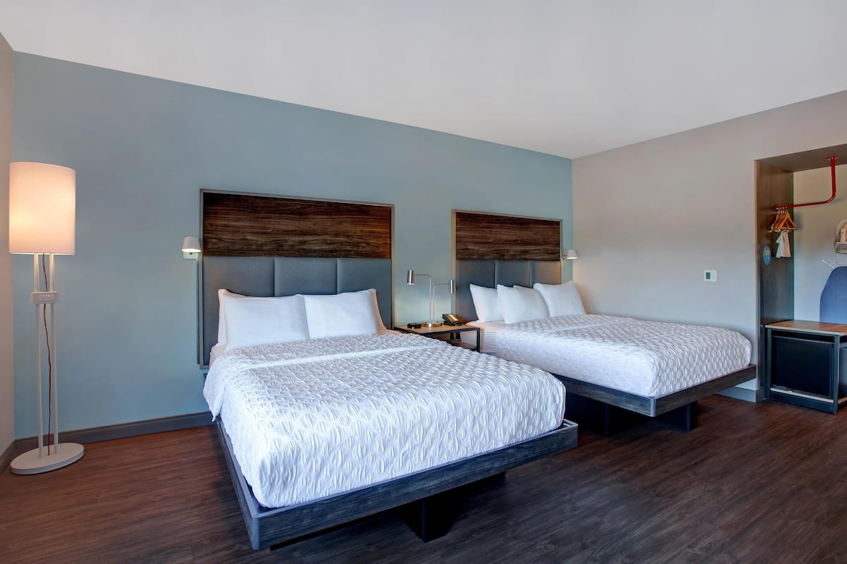 A hotel room with two beds, a floor lamp, a nightstand, and a mirror.