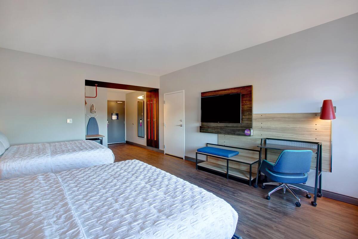 A hotel room with two beds, a desk, a chair, a TV, and a red lamp.