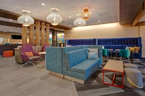 A modern lounge area with seating arrangements, including a blue sofa and chairs, and a small table. - Tru by Hilton Alcoa Knoxville Airport (Alcoa)