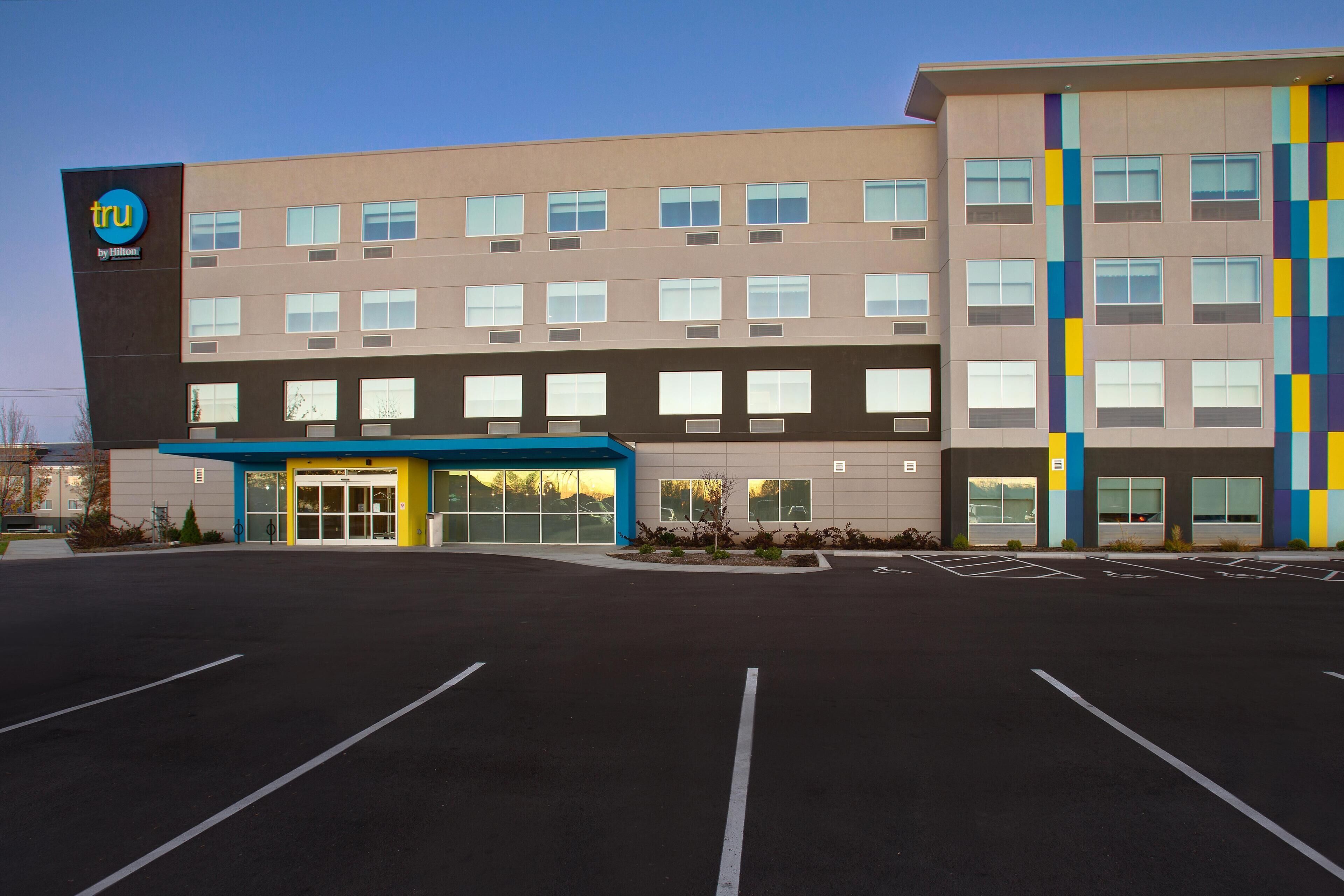 Ein modernes Hotel mit flacher Fassade, zahlreichen Fenstern und einem Parkplatz.