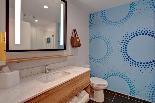 Un baño con un espejo grande, un lavamanos, un inodoro y una pared con un estampado azul a puntos.