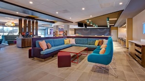A spacious lobby with a large sectional sofa, a red ottoman, and a blue armchair. There are multiple tables and a bar area in the background. - Tru by Hilton Alcoa Knoxville Airport (Alcoa)