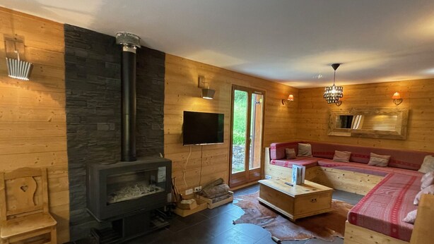 Un acogedor interior de cabaña con chimenea de piedra, paredes de madera, un sofá y un televisor.