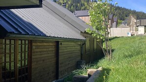 Un edificio rústico de madera con techo metálico, un pequeño porche y un área verde con un árbol.