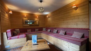 Interior acogedor de una cabaña con pared de madera, un amplio sofá en forma de L, una mesa de centro de madera y un espejo colgado.