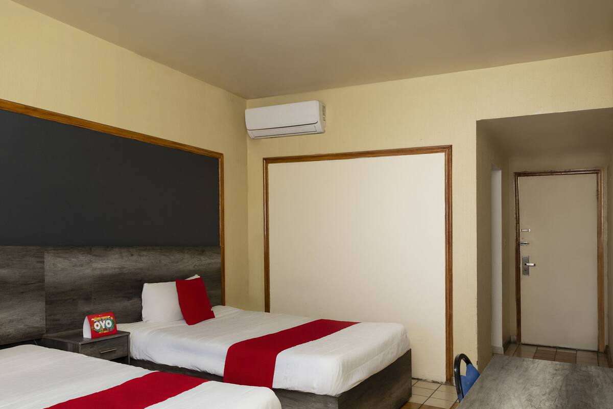 A hotel room with two beds, a nightstand, an air conditioning unit, and a door.