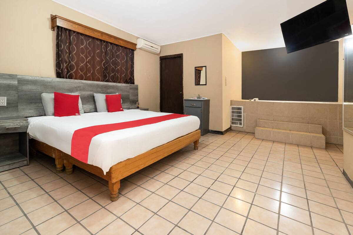 A hotel room with a large bed, a bedside table, a wardrobe, a bathroom with a shower, and a TV mounted on the wall.