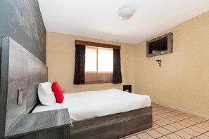 Un dormitorio con una cama, un televisor montado en la pared, una ventana con cortinas y piso de baldosas.