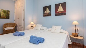 A hotel room with two beds, a wicker chair, and two wall-mounted lamps. - Port Pals "Summer Vibes" by Interhome (Pals)