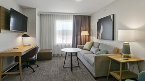 A hotel room with a desk, a sofa, a round table, and a TV mounted on the wall. - Staybridge Suites Atlanta Ne - Duluth by IHG (Duluth)