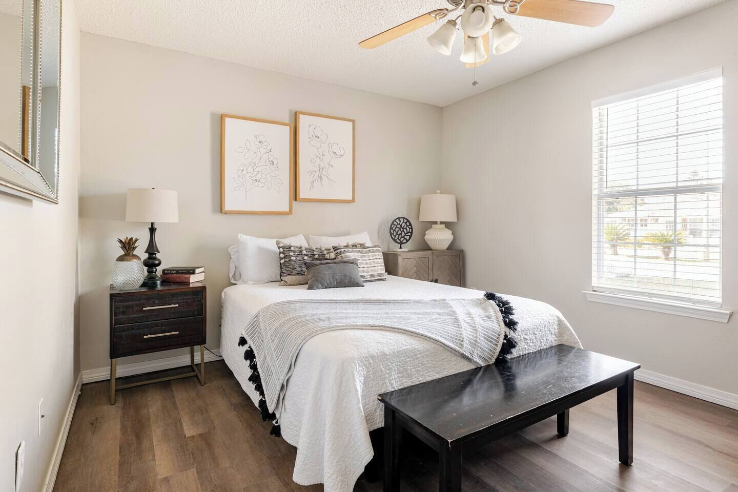 A bedroom with a bed, bedside tables, a bench, a ceiling fan, and a window with blinds.