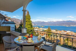 A balcony with wicker furniture, a table set with breakfast, and a scenic view of mountains and a lake. - La Rosa Dei Venti Stresa Lake View Terrace, Stresa, Italy (Stresa)