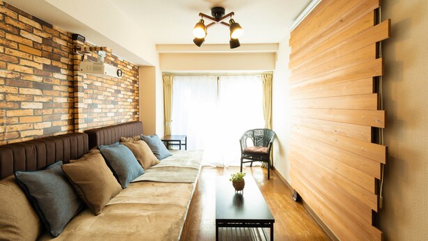 A modern living room with a brick wall, a wooden slat wall, a sofa with cushions, a coffee table, and a chair. - GrandTree Yokohama Station (Yokohama)