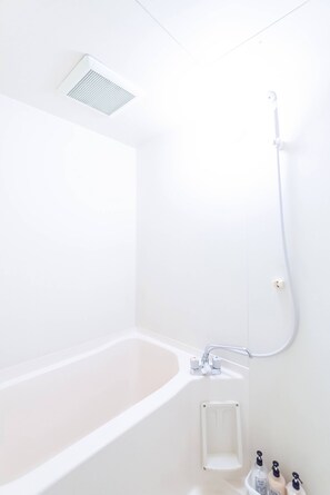 A white bathroom with a bathtub, a shower, and a small shelf with toiletries. - GrandTree Yokohama Station (Yokohama)
