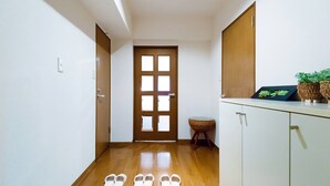 A hallway with a wooden floor, a door with glass panels, a small wicker basket, and a white cabinet with a plant on top. - GrandTree Yokohama Station (Yokohama)