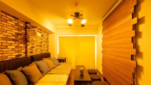 A modern hotel room with a brick wall, a wooden panel wall, a bed with multiple pillows, a small table with a vase, and a ceiling fan. - GrandTree Yokohama Station (Yokohama)