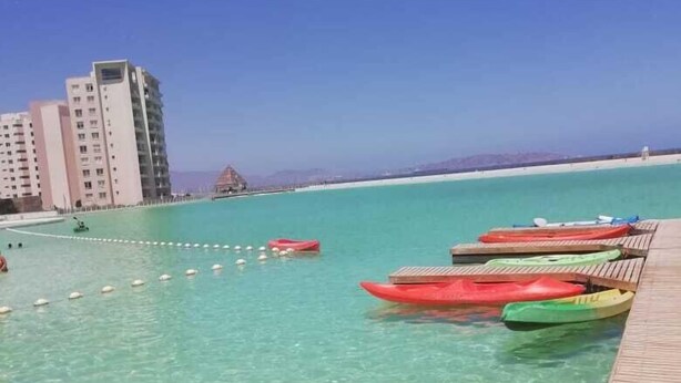 A clear turquoise pool with kayaks lined up on a wooden deck, overlooking a beach and buildings. - Beachfront Spectacular New Apartment sleeps up to 8 - Laguna del Mar (La Serena)