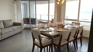 A dining area with a large table set for six, surrounded by chairs, and a sofa in the adjacent living area. - Beachfront Spectacular New Apartment sleeps up to 8 - Laguna del Mar (La Serena)