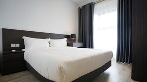 A hotel room with a large bed, dark wood headboard, a bedside table with a lamp, and a window with curtains. - The First Stay Hotel (Phung Cong)