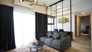 A modern living room with a grey sofa, black and white patterned pillows, a coffee table, and a large window with curtains. - The First Stay Hotel (Phung Cong)