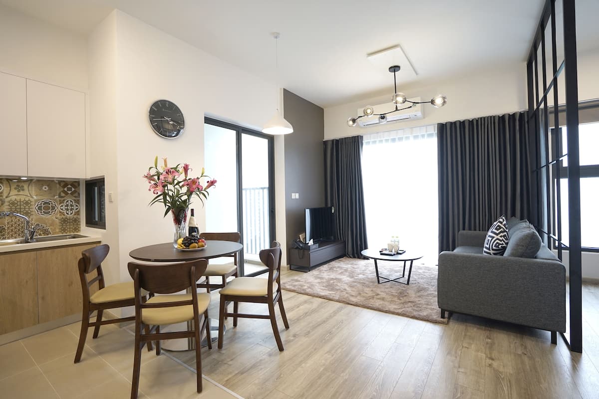 Uma sala de estar moderna com um sofá cinzento, uma mesa de jantar com cadeiras, uma televisão e uma janela grande com cortinas.