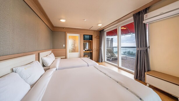 A hotel room with two beds, a TV, a desk, and a large window with a view of the sea. - Benikea San & Bada Jumunjin Resort (Gangneung)