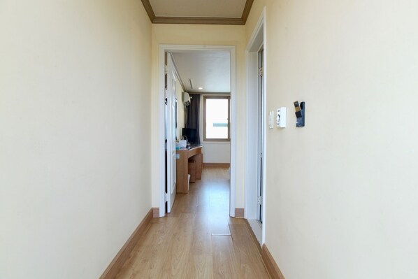 A narrow hallway with wooden flooring, leading to a room with a desk and chair.