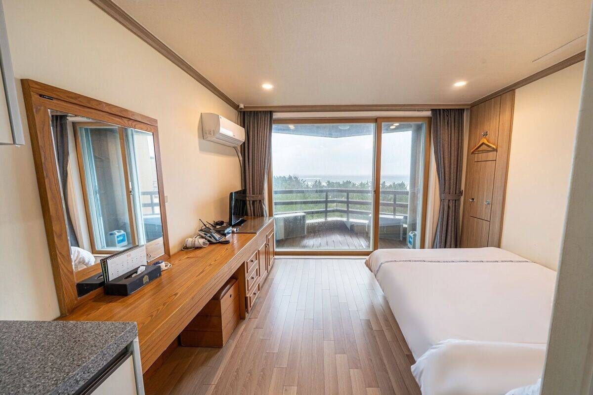 Ein Hotelzimmer mit einem großen Bett, einem Holztisch, einem Spiegel, einem Fernseher und einem Balkon mit Blick.