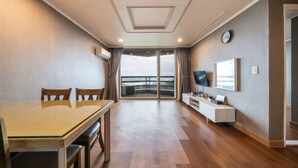 A hotel room with a dining table, chairs, a TV, a clock, and a view of the outside. - Benikea San & Bada Jumunjin Resort (Gangneung)