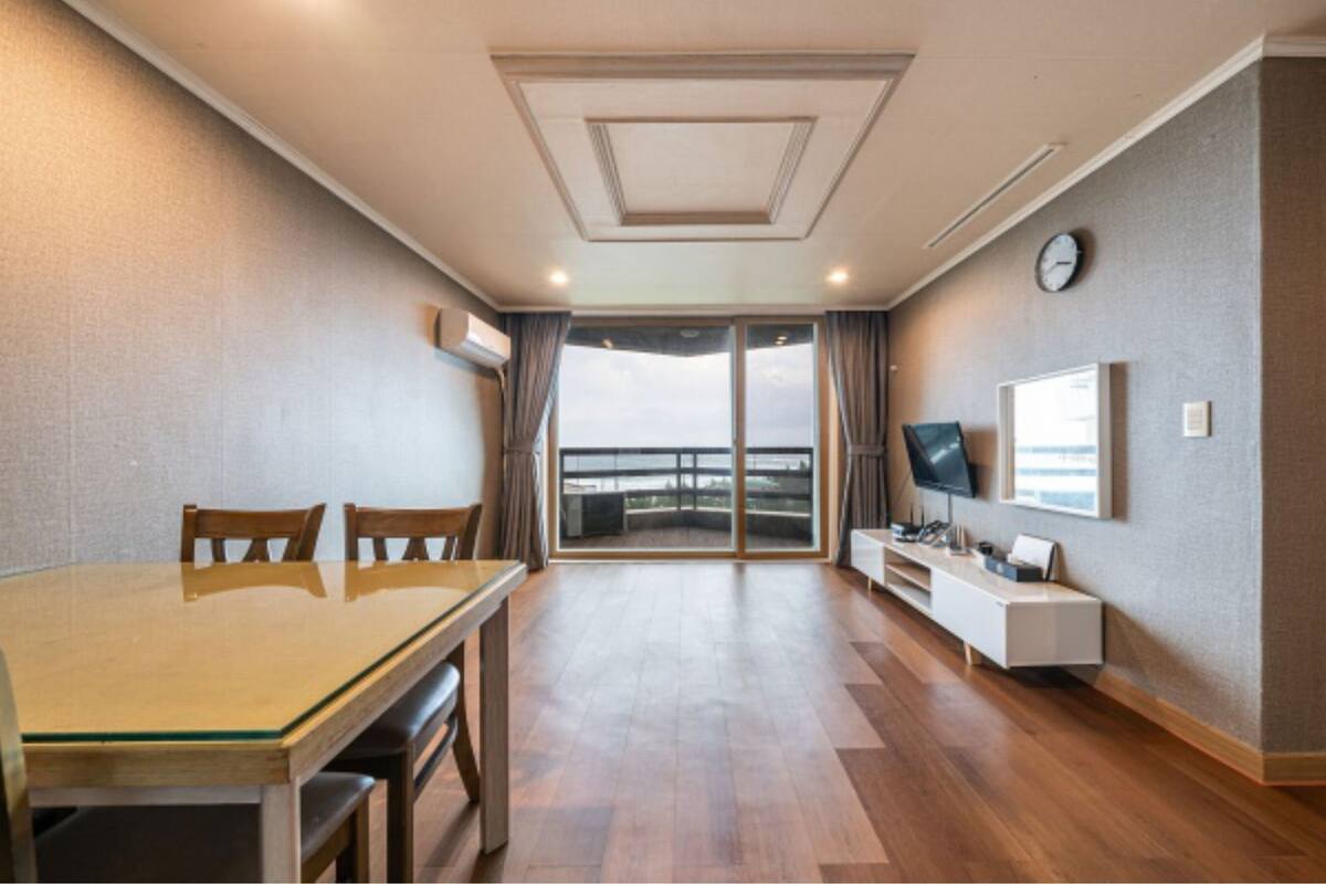 Ein Hotelzimmer mit Esstisch, Stühlen, Fernseher, einer Uhr und Blick ins Freie.