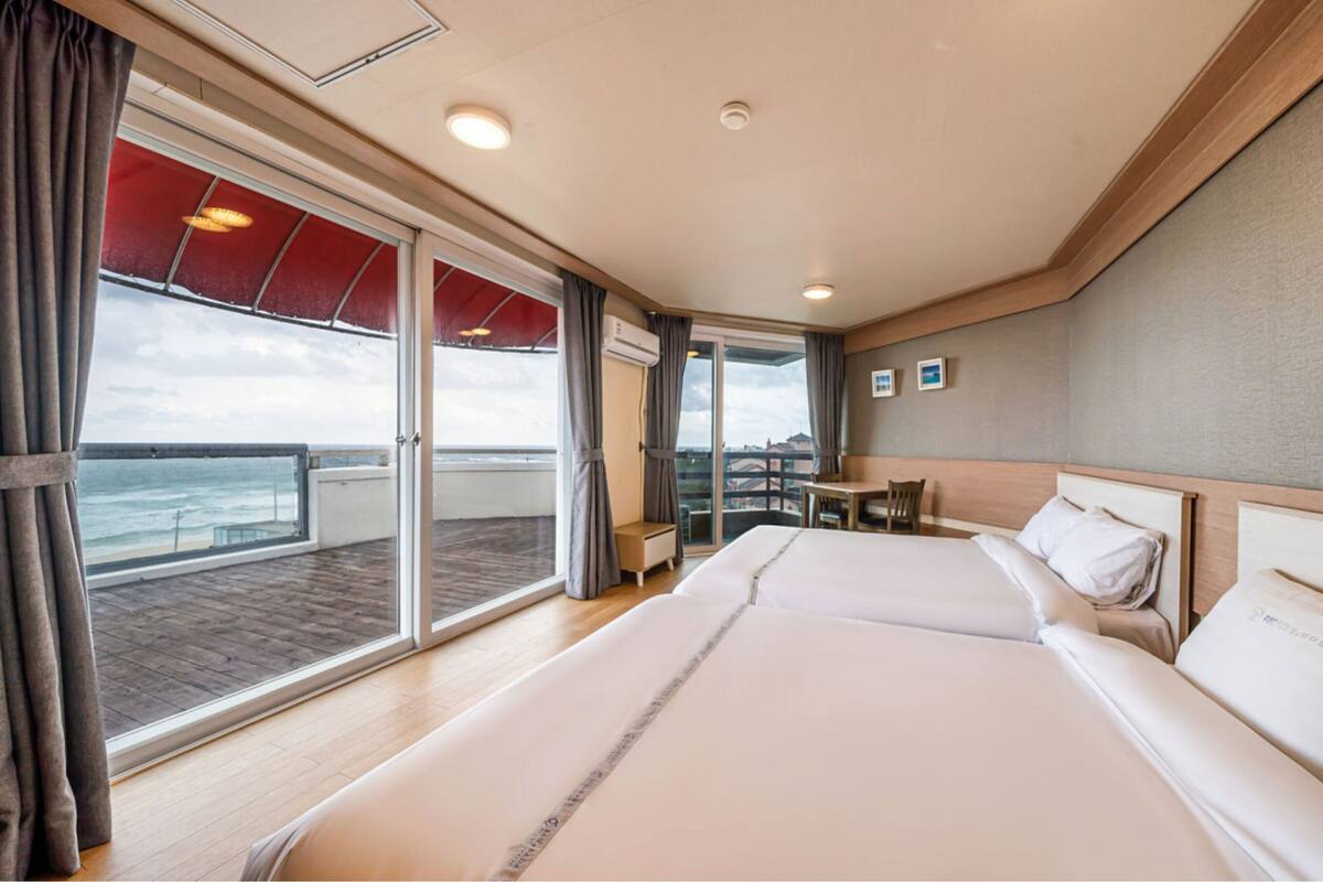 Ein Hotelzimmer mit einem großen Bett, einem kleinen Tisch und Meerblick durch eine Schiebetür.