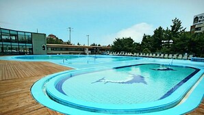 A swimming pool with a wooden deck area, surrounded by lounge chairs and a building with large windows. - Benikea San & Bada Jumunjin Resort (Gangneung)