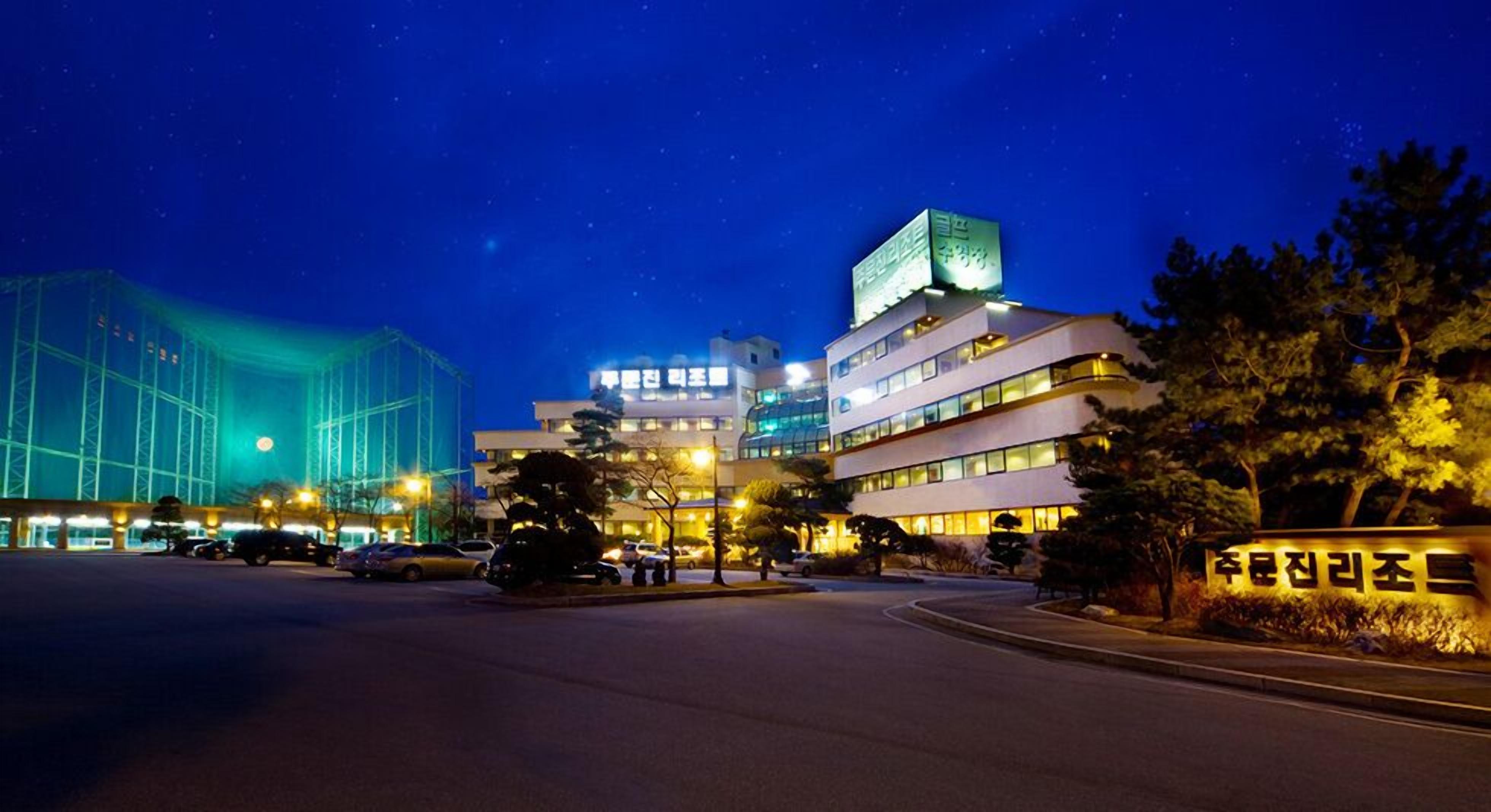 A modern hotel with a multi-story structure, illuminated signage, and a parking lot at night.