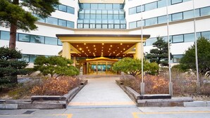 A modern building with a covered entrance, surrounded by landscaped areas with trees and shrubs. - Benikea San & Bada Jumunjin Resort (Gangneung)
