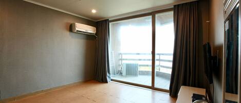 A hotel room with a large sliding glass door to a balcony, a flat-screen TV, and a desk with a laptop and a power strip.