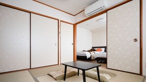 A room with tatami flooring, a low table, and a bed with a patterned headboard.
