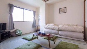 A room with tatami mats, a sofa, a TV, and a small table with a picture frame.