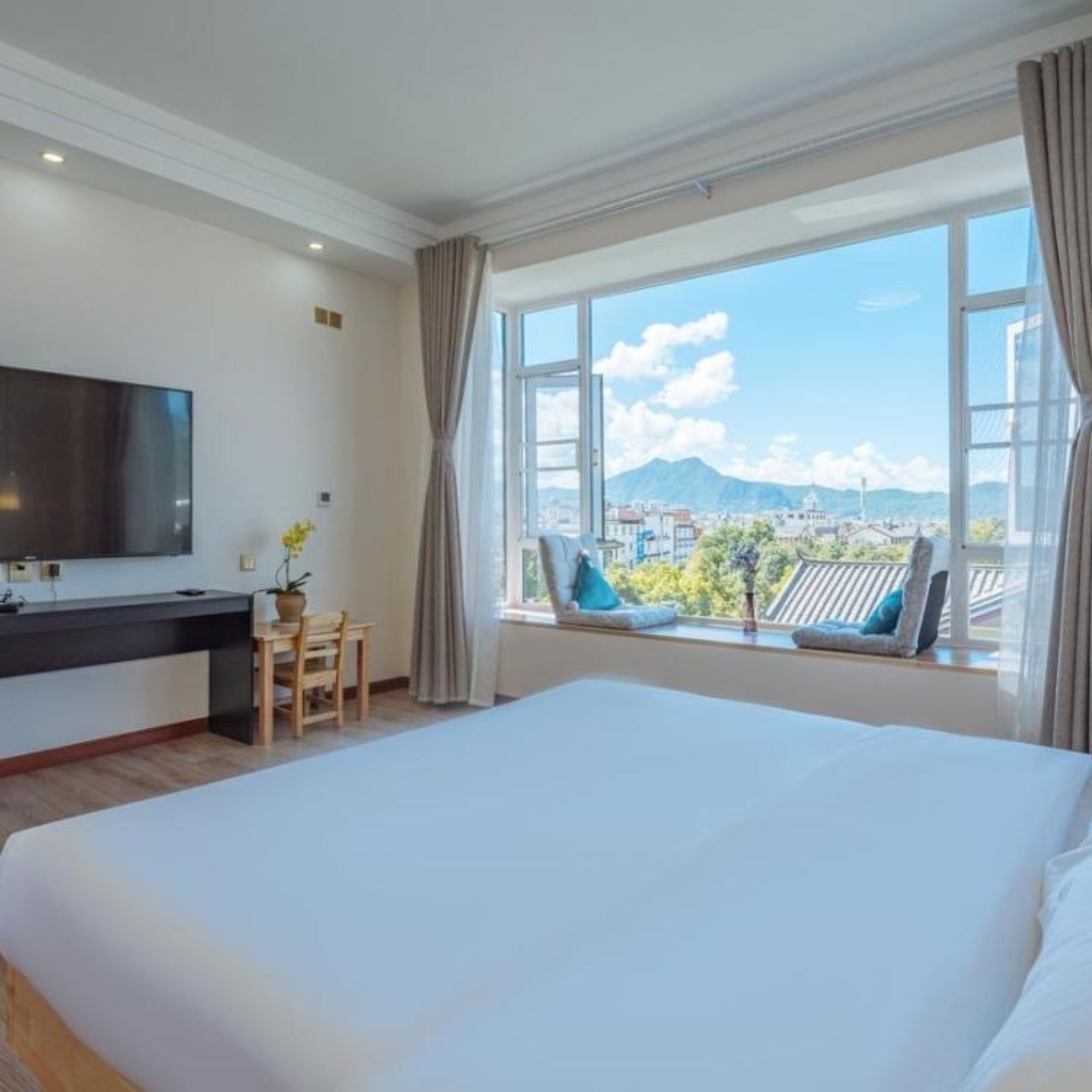 A hotel room with a bed, a desk with a chair, a TV, and a window with a city view.