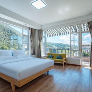 A bedroom with a large bed, a sofa, and a view of a mountainous landscape through large windows.