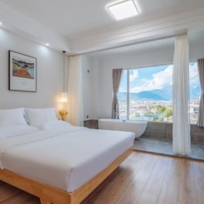 A hotel room with a large bed, a bathtub, and a window with a city and mountains view.