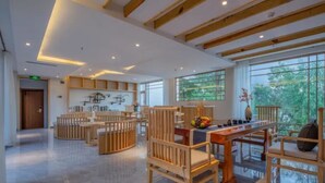 A spacious, modern interior with wooden furniture and large windows offering natural light and views of greenery.