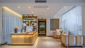 A modern reception area with a wooden reception desk, a glass door leading to a hallway, and a seating area with a wooden bench and cushions.