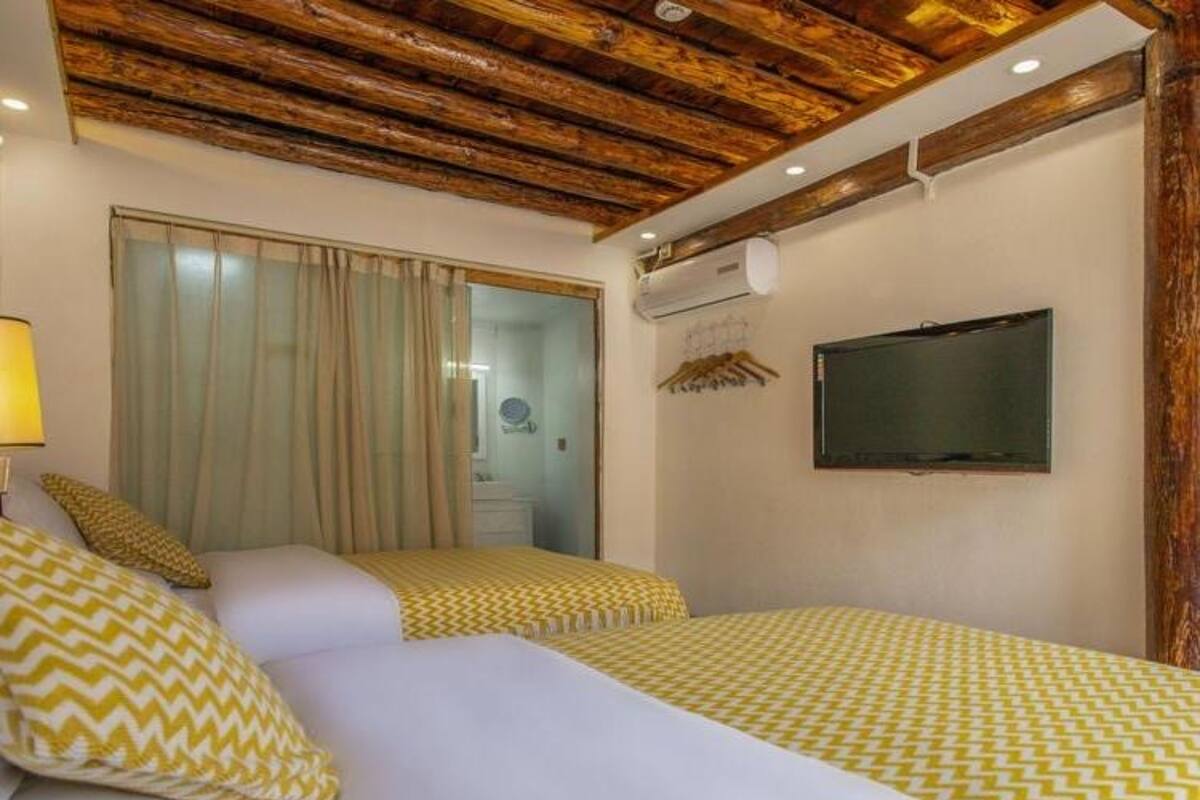 Habitación de hotel con dos camas, techo de madera, televisor y baño visible a través de una puerta de cristal.
