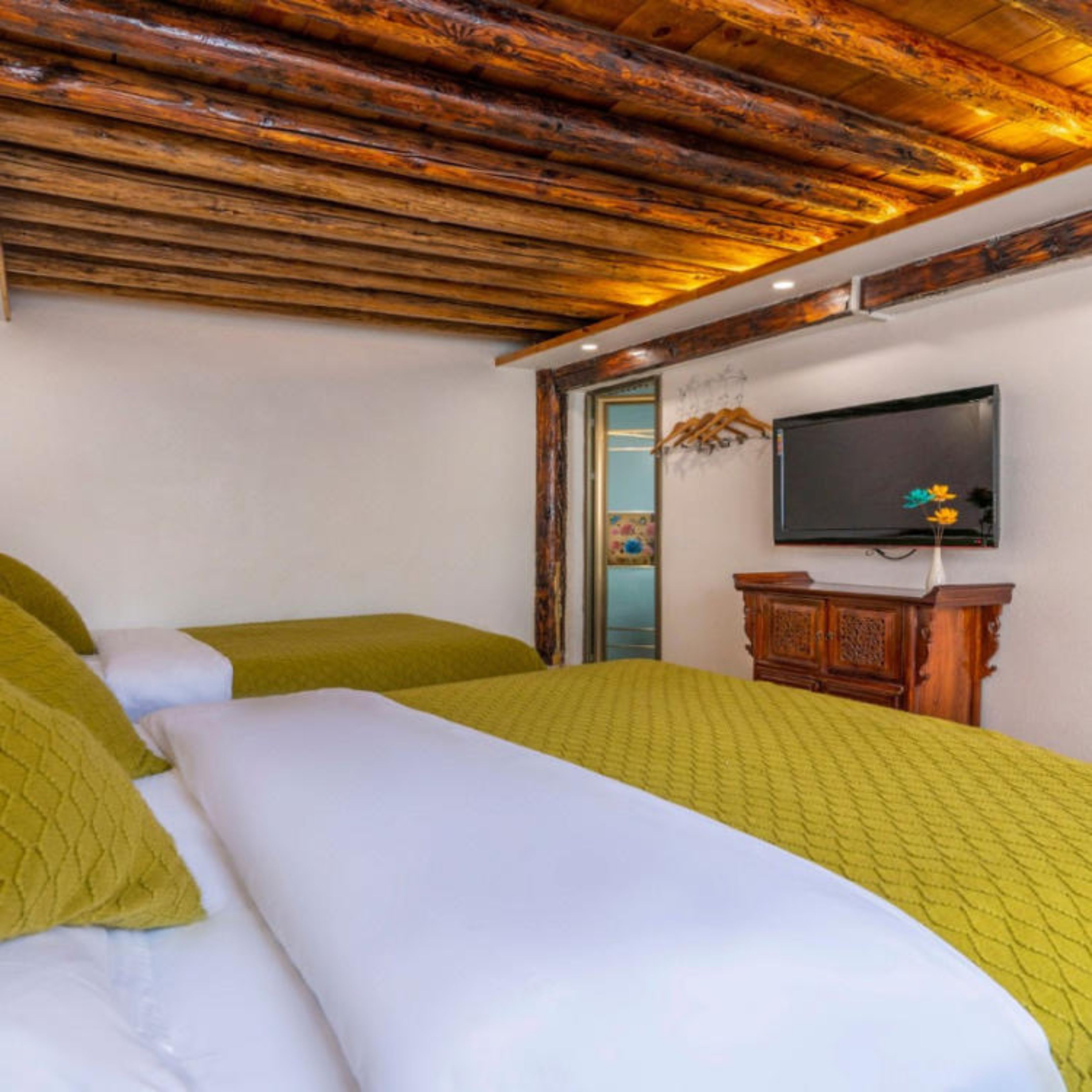 A hotel room with two beds, wooden ceiling beams, a television, and a wooden cabinet.
