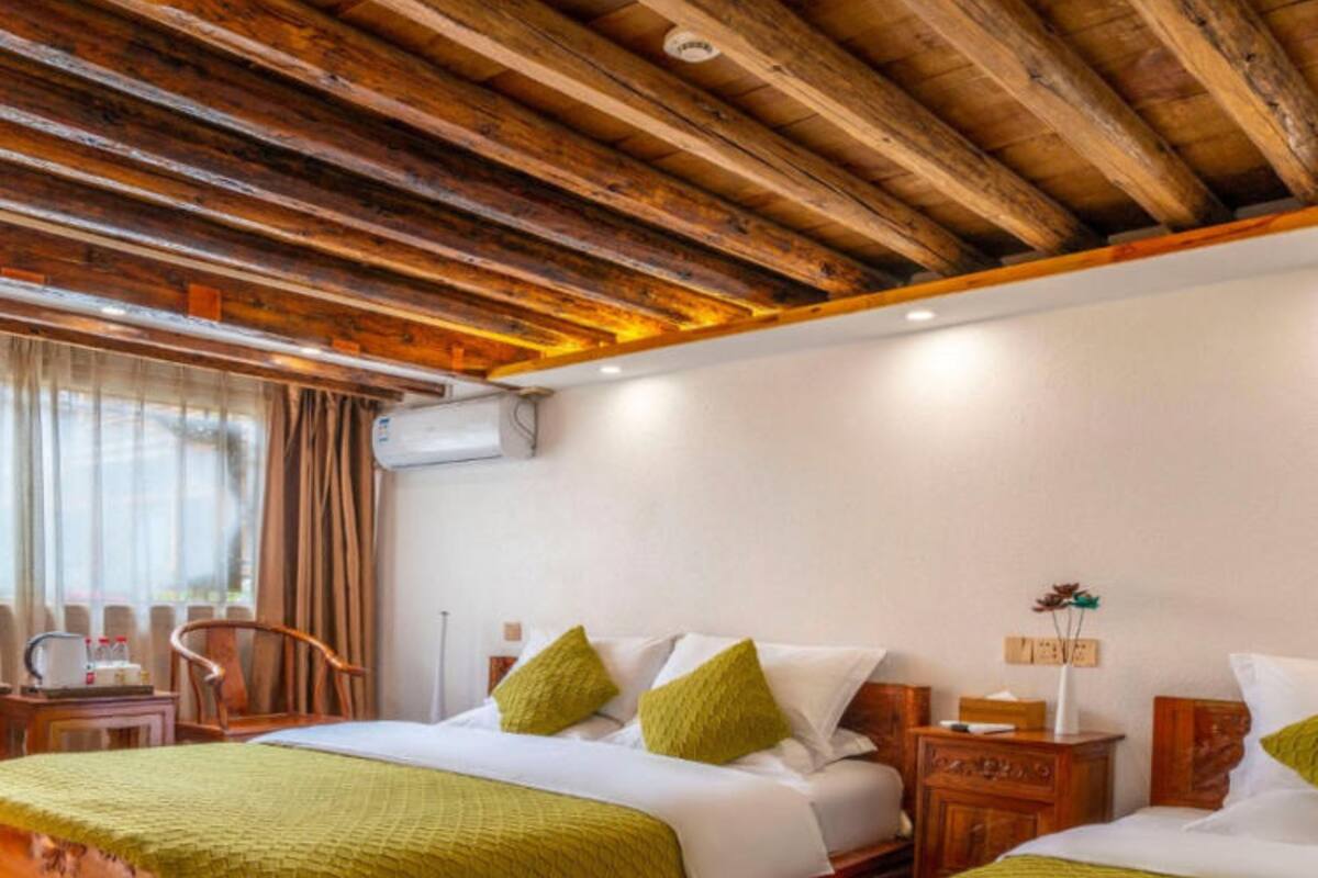 Habitación de hotel con dos camas, cabeceros y techo de madera, una ventana con cortinas y una mesita de noche con lámpara.